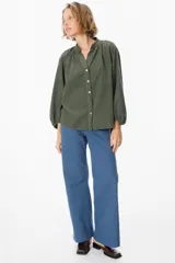 Camisa de pana color verde oliva, con cuello mao, cierre frontal de botones y mangas largas abullonadas con puños elásticos.