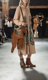 Botas de cuero color marrón tierra con taco medio, detalles de costuras artesanales en el borde superior y un aplique lateral con diseño geométrico pintado en tonos turquesa y cobrizo.