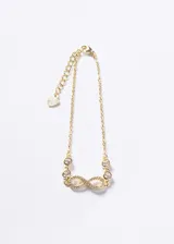 Pulsera de cadena fina con baño de oro 18k, que presenta un dije central en forma de símbolo de infinito decorado con pequeñas zirconias y dos puntos de luz a cada lado. Incluye una cadena de extensión con un pequeño dije en forma de corazón.