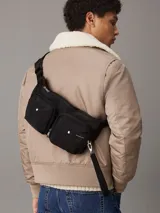 Riñonera negra de poliéster reciclado con correa ajustable con clip, cierre de cremallera en la parte superior y dos bolsillos exteriores en la parte delantera con anillas en D. Se pliega y se cierra con cremallera para crear una cartera para la muñeca.