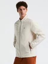 Campera rompevientos color crema con cierre frontal, cuello alto, capucha oculta, puños elásticos y bolsillos laterales con cierre.