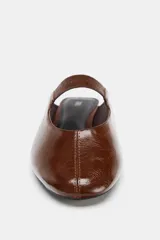 Zapato plano tipo bailarina destalonada, color marrón brillante, con tira elástica en el empeine y punta redonda.