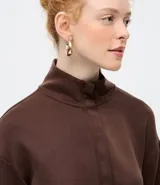Buzo de modal color marrón, de manga larga, con cuello alto estructurado y cierre frontal parcial con cremallera. Presenta diseño confortable con costuras pespunteadas en el frente y puños y ruedo ajustados.
