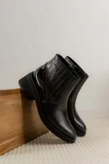 Bota corta de cuero negro con textura de reptil en el panel lateral y acabado liso en la puntera. Cuenta con taco cuadrado bajo y cierre lateral.
