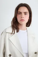 Campera estilo trench corta color beige, con solapas amplias, cierre cruzado de doble botonadura con botones oscuros y diseño holgado.