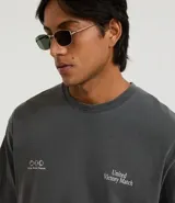 Remera de algodón de corte boxy, color gris oscuro con efecto desteñido/vintage. Presenta un estampado minimalista en blanco en el pecho con tres círculos y texto a la derecha que dice "United Victory Match".