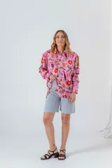 Camisa de seda blanca con estampado de flores rojas, palmeras, piñas y tucanes. Tiene cuello clásico, mangas largas y corte recto.