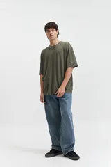 Remera oversize verde militar de manga corta y escote redondo, con estampado trasero de una cara sonriente amarilla con detalles en negro y texto "mistral 1976co".