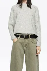 Sweater de punto color gris melange, confeccionado en una mezcla de lana y alpaca. Presenta un diseño de corte recto con escote redondo, mangas largas tipo murciélago con puños anchos y detalles de piedras brillantes aplicadas en toda la prenda.