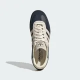 Zapatillas Adidas Samba OG con exterior de cuero azul marino y detalles en gamuza beige. Presentan las icónicas tres tiras laterales, suela de goma color marrón y el nombre del modelo en letras doradas.