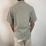 Camisa de manga corta confeccionada en muselina de textura arrugada, con cuello solapa, cierre frontal de botones y pequeño bordado en el pecho.