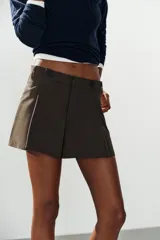 Short de tiro alto color marrón, con pliegues frontales y detalle de botones decorativos en la cintura. Cuenta con bolsillos laterales y cierre frontal con cremallera y gancho metálico.
