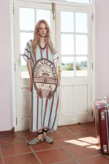 Túnica larga celeste con rayas verticales marrones y estampado central con el logo de un hotel. Tiene cuello en V con detalle de puntilla y tajos laterales.