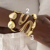 Set de tres pulseras doradas. La primera y la tercera son pulseras rígidas con eslabones irregulares, la segunda es una pulsera rígida con múltiples hilos.