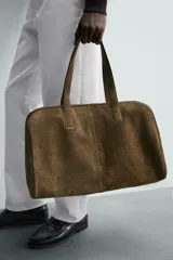Bolso de viaje tipo duffel de piel con acabado serraje, color verde oliva. Presenta dos asas de mano y un compartimento principal con cierre de cremallera e imanes. El interior incluye un bolsillo con cremallera y un bolsillo plano.