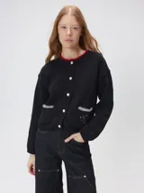 Cardigan de algodón grueso en color rojo, con cuello redondo y cierre frontal de botones grandes. Presenta bolsillos cuadrados en el bajo con detalles de pelo sintético en los bordes y logo bordado en uno de ellos. Posee puños y ruedo elastizados con diseño holgado.