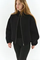 Campera negra de felpa con efecto neopreno, corte oversized y hombros caídos. Presenta cuello redondo, cierre frontal metálico, bolsillos delanteros insertados y elástico revestido en puños y bajo.