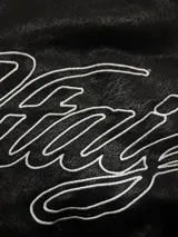 Campera de cuero sintético negro con diseño tipo bomber, cuello camisero y puños y ruedo elásticos. Presenta un bordado grande en la espalda con tipografía cursiva en color blanco.
