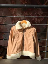 Campera color beige de cuero sintético con cuello, puños y ruedo de corderito blanco. Cierre frontal con cremallera.