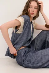 Top azul de corte holgado con detalles de encaje crudo en los hombros y pliegues frontales.