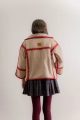 Chaqueta de paño reversible con diseño de cuadros en el interior. Presenta bordes con costuras decorativas en hilo rojo y mangas con puños vueltos que dejan ver el estampado interior.