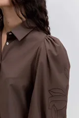 Camisa de color marrón con cuello clásico, mangas abullonadas y detalle de bordado floral en una de las mangas.