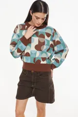 Sweater de tejido de punto con diseño geométrico multicolor en tonos marrón, celeste, verde y crudo. Presenta cuello redondo, mangas largas abullonadas y puños y ruedo elásticos en color marrón.