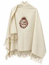 Ruana marfil de 100% lana merino con flecos en los bordes y detalle de bordado frontal en tono marrón que representa el escudo nacional.