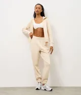 Pantalón jogger deportivo color beige, con cintura elástica, bolsillos laterales y puños ajustados en los tobillos. Presenta recortes canelados en los laterales que aportan textura al diseño.