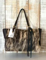 Cartera tipo tote con cuerpo central de piel con estampado animal print en tonos tierra y laterales de cuero liso marrón oscuro. Cuenta con doble asa de hombro ajustable con hebillas metálicas y detalle de flecos largos de cuero en uno de los laterales.