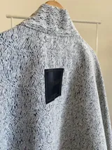 Ruana abierta con diseño estructurado y corte asimétrico, confeccionada en tela tipo tapiz con textura jaspeada en tonos grises.