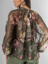 Camisa de seda italiana con estampado floral en tonos rosados, marrones y verdes. Presenta cuello alto con volados que caen en cascada sobre el frente y mangas largas abullonadas con puños ajustados.