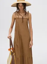 Vestido midi de denim color marrón, con corte holgado, breteles finos con lazos ajustables y detalle de volado en el ruedo.