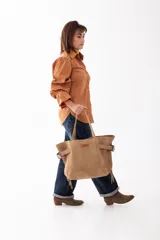 Bolso shopper de cuero descarne color tostado, con diseño de flecos laterales, hebillas metálicas decorativas y doble asa de hombro.