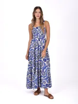 Vestido largo de corte holgado con estampado floral en tonos azul y blanco. Presenta escote cuadrado, cuerpo con frunces elásticos y falda con volados escalonados.