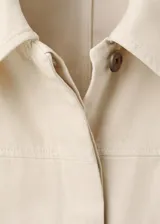 Chaqueta de algodón estilo tejano en color beige, con cuello camisero, manga larga, dos bolsillos de parche en el frente y cierre delantero de botones.