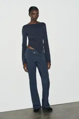 Camiseta de cuello barco y manga larga con diseño asimétrico en el bajo. Presenta un corte entallado con cierre lateral mediante cremallera oculta.