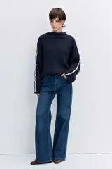 Sweater de punto acanalado en color azul marino, con cuello alto y detalle de costura decorativa en contraste blanco a lo largo de las mangas.