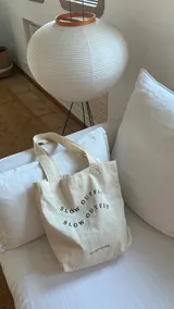 Tote bag color crudo con estampa negra con la frase "Slow Outfit" repetida.