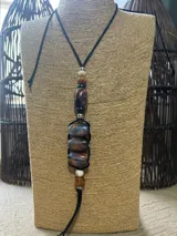 Collar largo con cordón negro ajustable, decorado con una serie de cuentas de resina en tonos marrones, azules y blancos, intercaladas con pequeñas esferas metálicas plateadas.