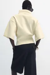 Jersey de punto color amarillo claro, con cuello subido, manga corta con hombreras y cintura entallada.