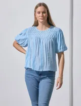 Blusa blanca de gasa marca Zac & Rachel, con frunces en la parte delantera, mangas cortas con puño elastizado, abertura central en la espalda y botón.