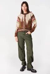 Cardigan clásico de largo medio color crudo, de manga larga, con cuello redondo, puños y ribetes en marrón con rayas blancas, y cierre frontal de botones marrones.