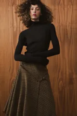 Falda midi de tiro medio con diseño asimétrico y acabados desflecados. Presenta un patrón de cuadros tipo príncipe de Gales en tonos tierra y cierre lateral con cremallera oculta.