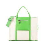 Bolso tipo tote de tela color crudo con detalles en cuero sintético verde. Tiene doble asa corta, correa larga regulable y extraíble, bolsillo frontal con cierre, cierre principal, bolsillo interno con cierre y dos bolsillos internos abiertos.