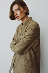 Blazer de corte recto confeccionado en tejido jacquard con diseño floral en tonos tostados. Presenta cuello mao, manga larga y cierre frontal mediante alamares decorativos. Incluye bolsillos de vivo en el delantero.