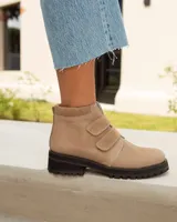 Botín corto de cuero color visón (beige/topo), con cierre de tres tiras de velcro en el empeine. Posee cuello acolchado de gamuza y suela de goma negra con relieve tractor.