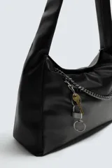 Bolso tipo bandolera de cuero sintético negro, con asa de hombro y detalle de cadena metálica plateada en el frente. Incluye un charm colgante con forma de llave.