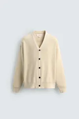 Cardigan de punto de algodón en color beige, con cuello en V, manga larga, puños y dobladillo acanalados, y cierre frontal con botones oscuros.