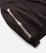 Buzo canguro marrón oscuro con capucha, cierre frontal completo y bolsillos, confeccionado en mezcla de algodón y poliéster con interior de felpa. Presenta una estampa en la espalda y mangas con diseño de huesos en tono beige claro con efecto desgastado.